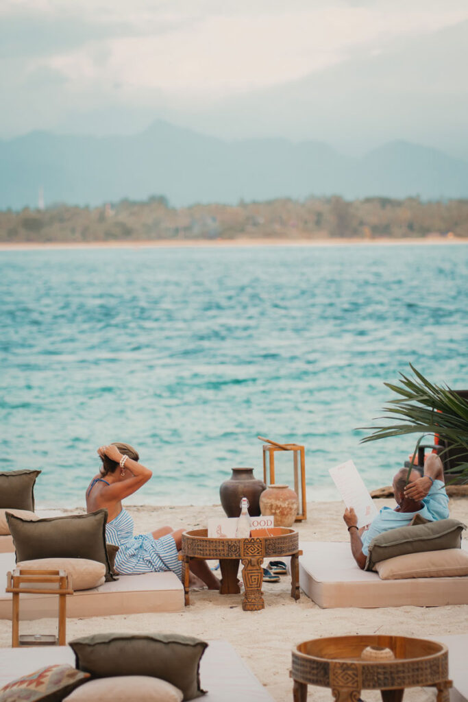 Guests relaxing on sunbeds at Bahia Gili Air with the turquoise sea and mountains visible across the water.