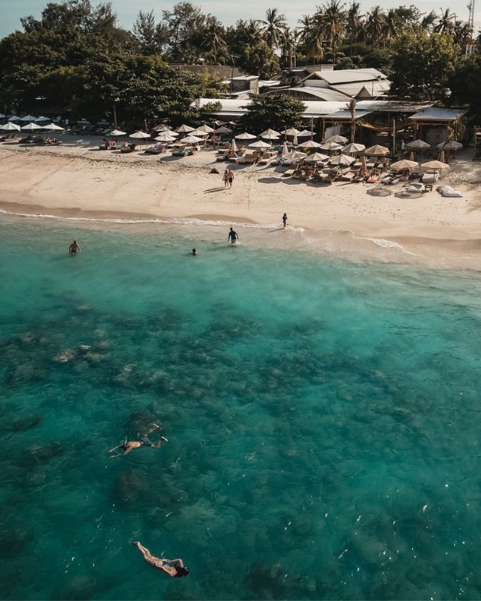 Aerial view of swimmers and snorkelers in turquoise water off Bahia’s beachfront in Gili Air.